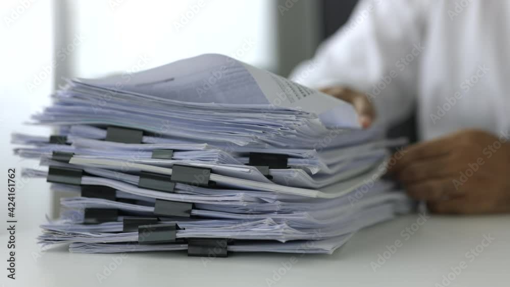 A young business man in a suit is managing paperwork in the office. Many paperwork that is not finished. Documents in the company about finance and information of the company.