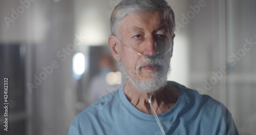 Sick elderly dying man with nasal oxygen tube in hospital looking out window