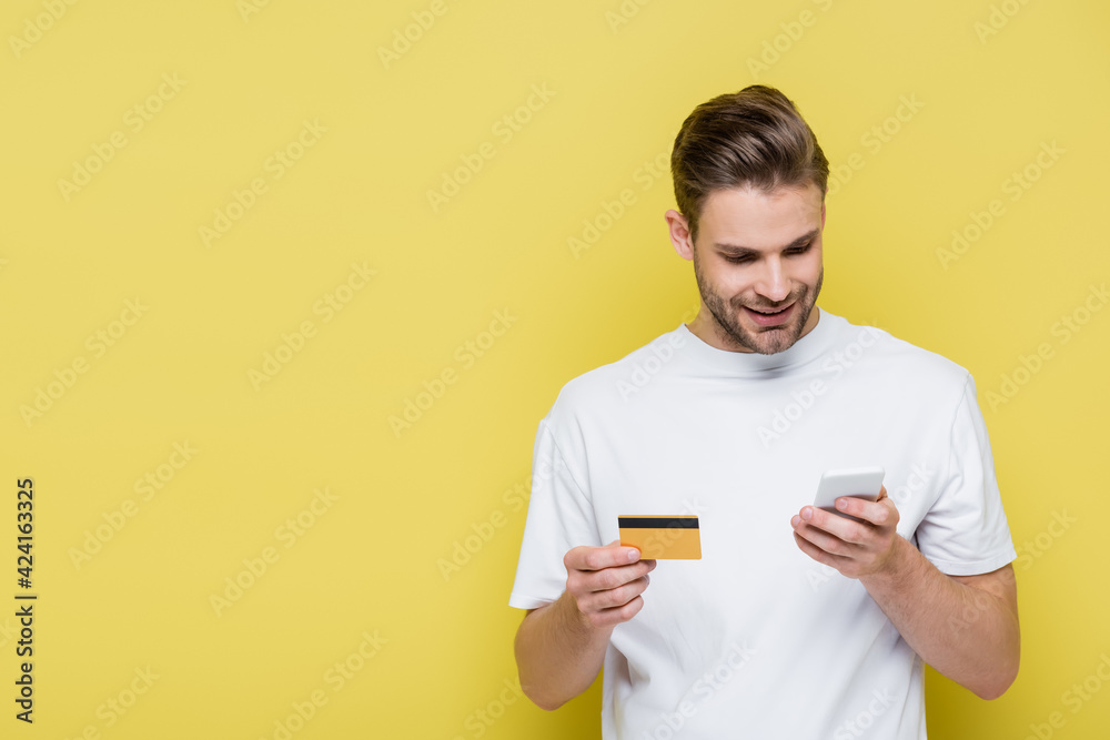 positive man chatting on smartphone while holding credit card on yellow positive man chatting on smartphone while holding credit card on yellow