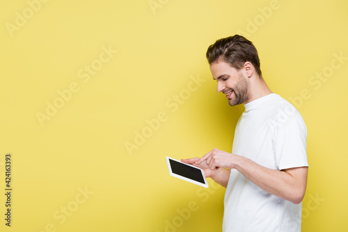 side view of smiling man pointing at digital tablet with blank screen on yellow