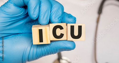 ICU Intensive care unit - word from wooden blocks with letters holding by a doctor's hands in medical protective gloves. Medical concept.