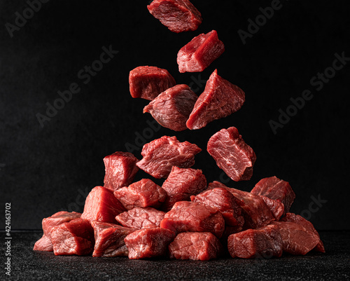 Cubes of raw beef falling over black background