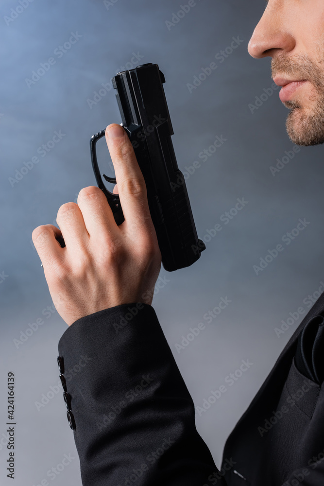 cropped view of businessman holding gun on grey background with smoke - obrazy, fototapety, plakaty 