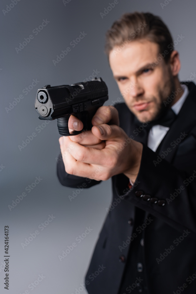 businessman in black suit aiming with gun on grey, blurred background businessman in black suit aiming with gun on grey, blurred background