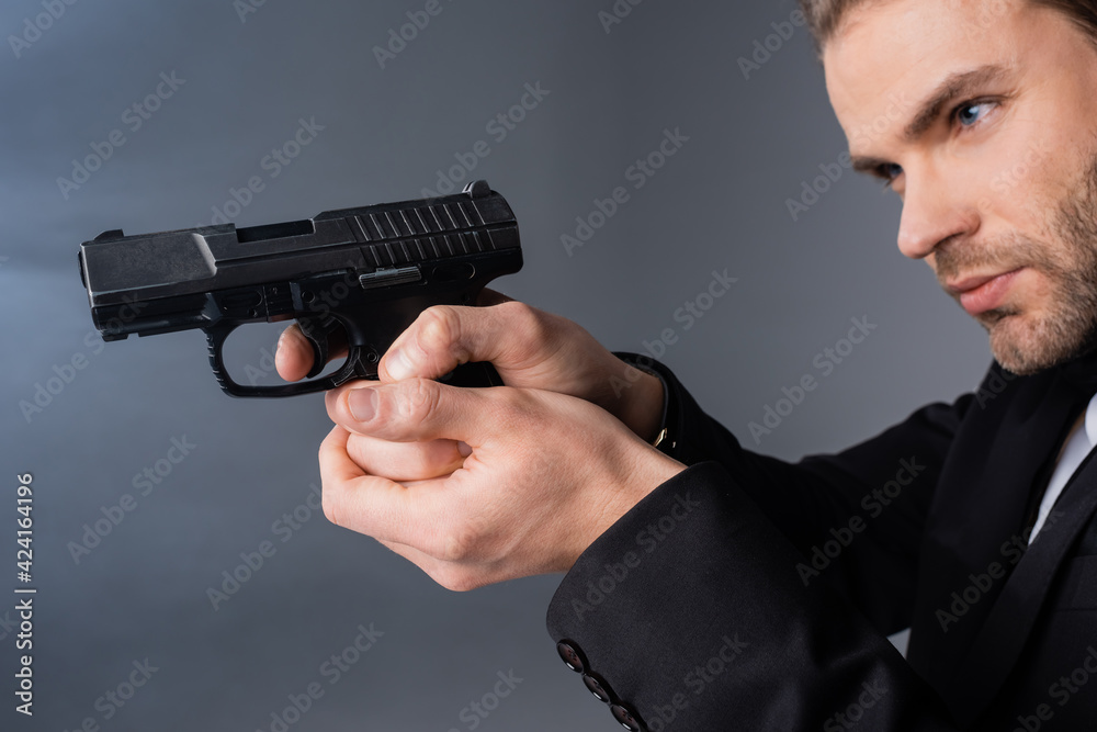 young businessman aiming with gun on grey background with smoke - obrazy, fototapety, plakaty 