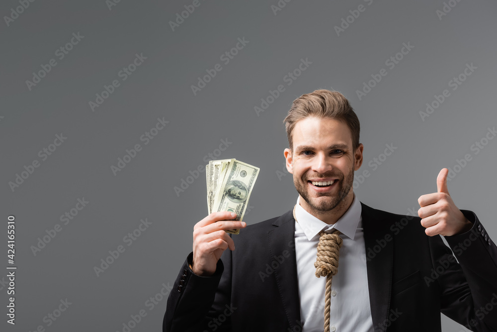 cheerful businessman with tie made of rope holding dollars and showing like isolated on grey cheerful businessman with tie made of rope holding dollars and showing like isolated on grey