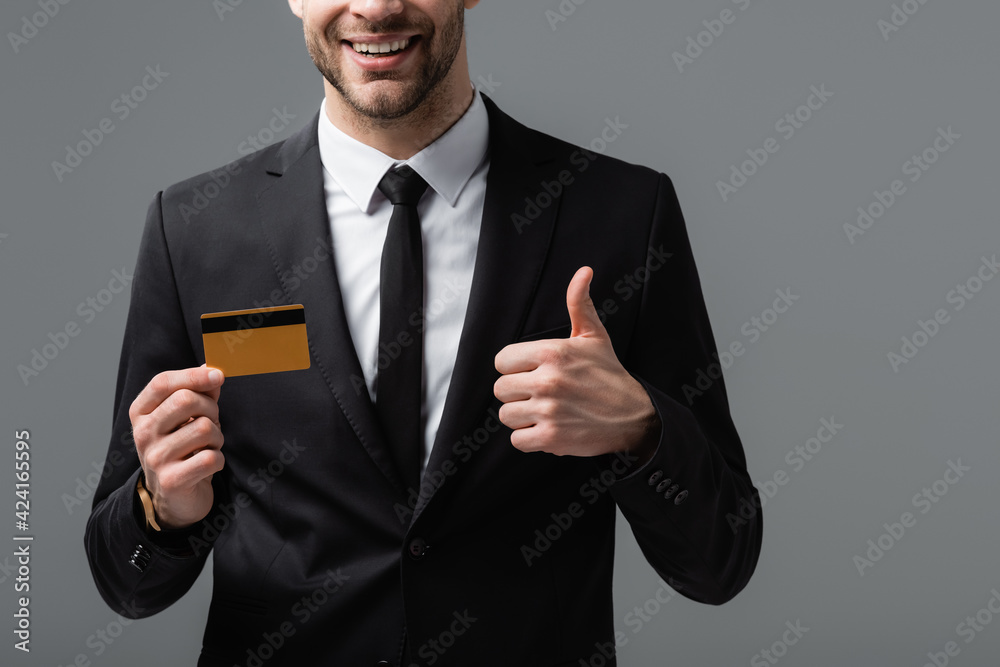 partial view of joyful manager showing thumb up and credit card isolated on grey partial view of joyful manager showing thumb up and credit card isolated on grey