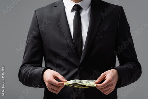 partial view of businessman in formal wear holding dollars isolated on grey