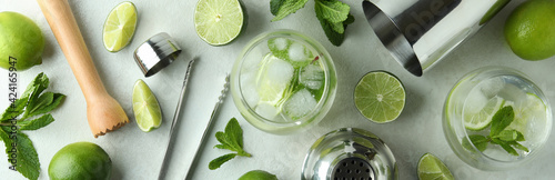 Glass of mojito cocktail and ingredients on white textured table