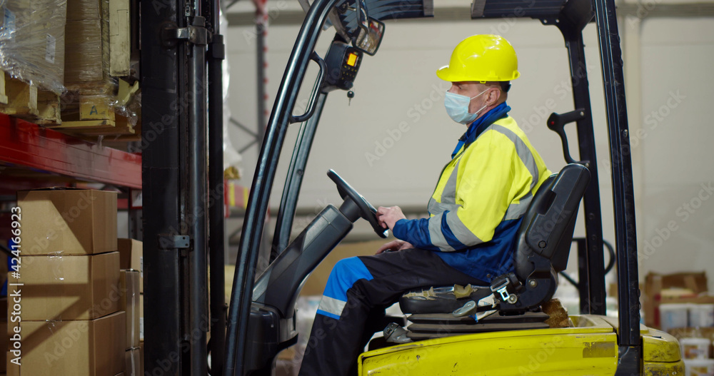 Forklift driver in safety mask loading cardboard boxes pallet on truck at warehouse Forklift driver in safety mask loading cardboard boxes pallet on truck at warehouse