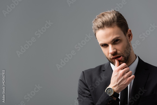 pensive businessman looking at camera while touching lip isolated on grey