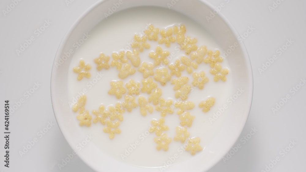 Kid corn flakes in a milk in a white bowl, top view