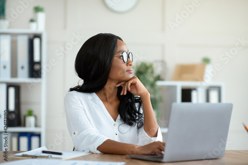 Millennial black entrepreneur daydreaming in front of laptop at contemporary office © Prostock-studio