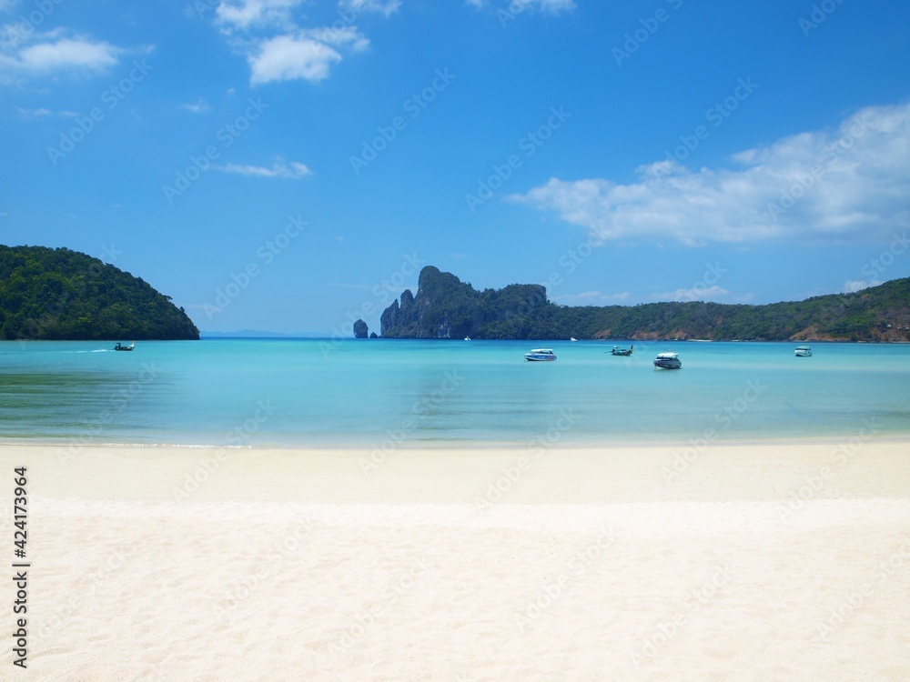 Small deserted beach in a sea bay. White clean sand, transparent bright turquoise water, rocks covered with green forest on the horizon. Boats on the calm water. Thailand, tropical resort. Beautiful