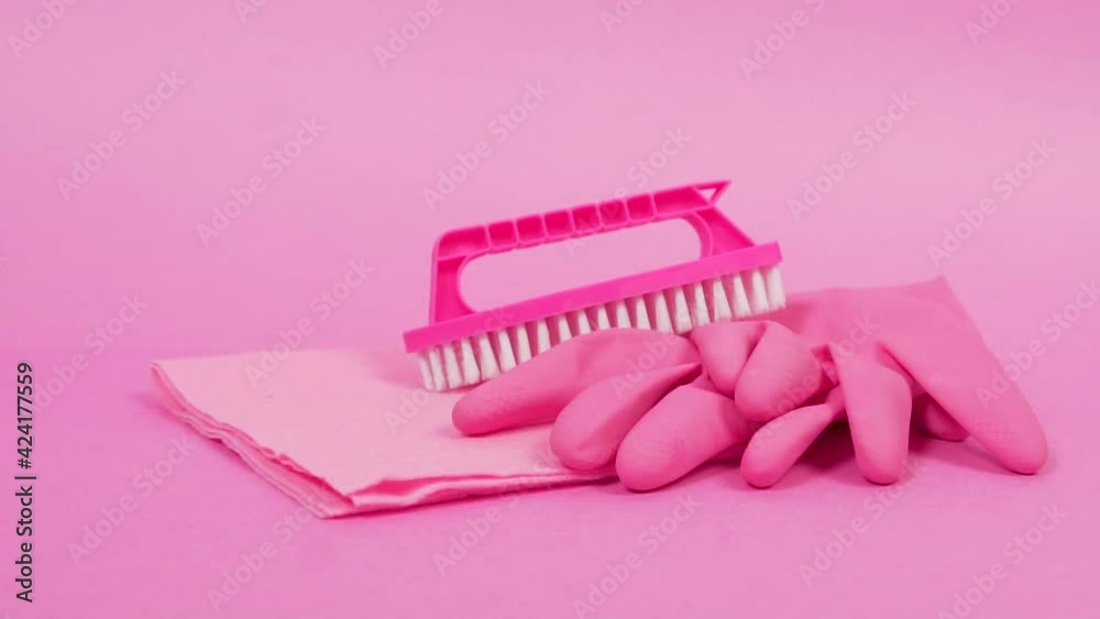 Close-up of a duster, rubber gloves, and a brush. Pink bright background. Tools for manual cleaning of the house.