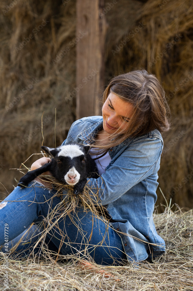 Beautiful girl playing with a lamb in the hay on the farm