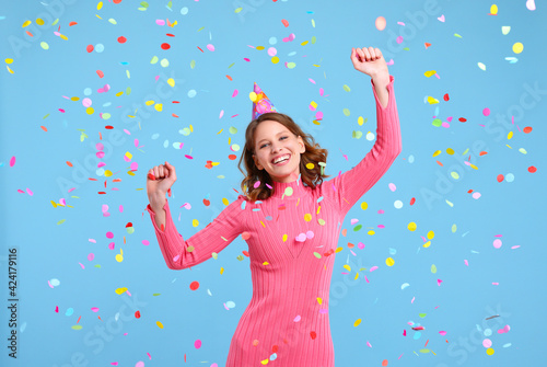 Delighted female in party hat dancing under confetti
