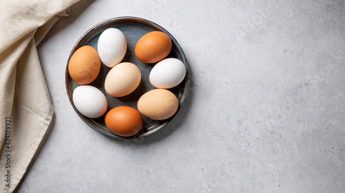 Colorful chicken eggs in bowl on gray background. Top view, copy space.