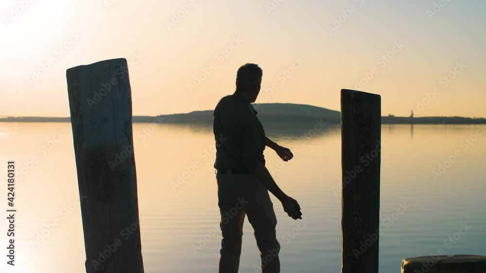Frustrated and angry man talking on smartphone and throwing it in the lake. Silhouette of an annoyed businessman standing on a pier and throwing his phone in the water. Slow-motion, 4K.