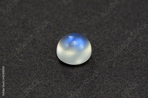 Natural adularia blue sheen round cabochon moonstone. Loose gem on gray textured leather background. Feldspar mineral group. Semiprecious gemstone not common relatively rare and expensive specimen