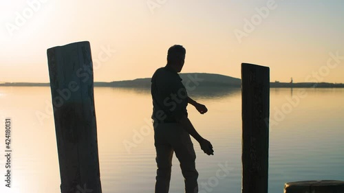 Frustrated and angry man talking on smartphone and throwing it in the lake. Silhouette of an annoyed businessman standing on a pier and throwing his phone in the water. Slow-motion, 4K.