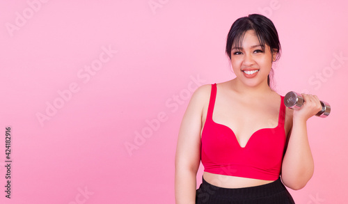 Exercise bodybuilding diet healthy care concept. Chubby obesity plus- size smile woman holding dumbbells workout for weight loss while standing over isolated pink background.