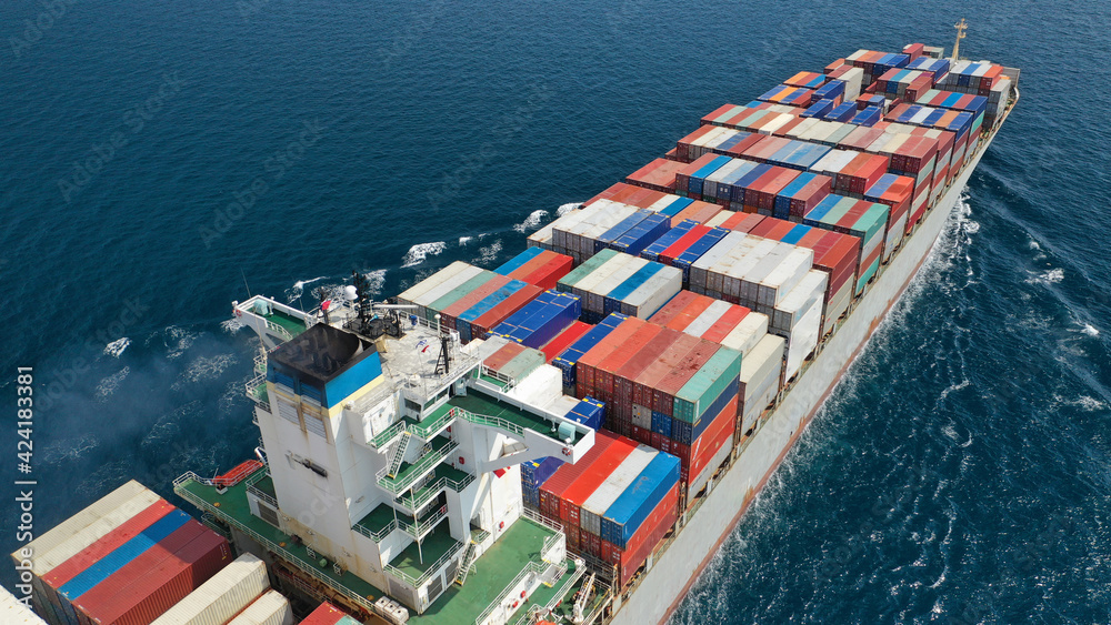 Fototapeta premium Aerial drone photo of huge container tanker ship carrying truck size colourful containers in deep blue open ocean sea