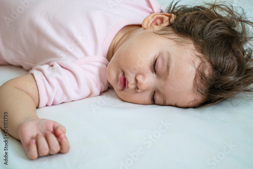 Murais de parede Little baby girl 12 months wearing pink cloth sleeping on white bed at home