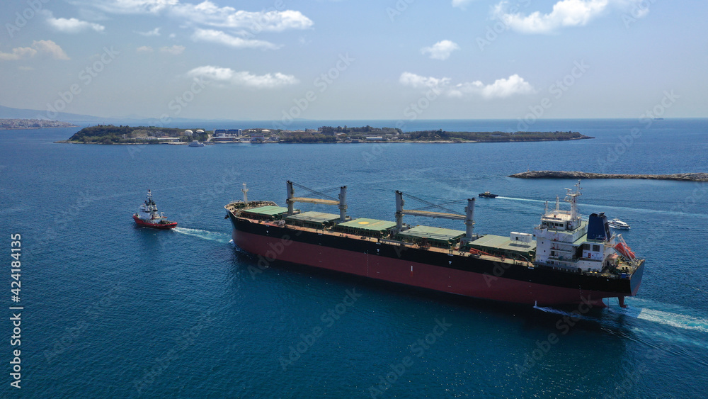 Aerial drone photo of cargo carrier tanker leaving industrial port of Perama with the help of tug boats for Mediterranean destination, Attica, Greece
