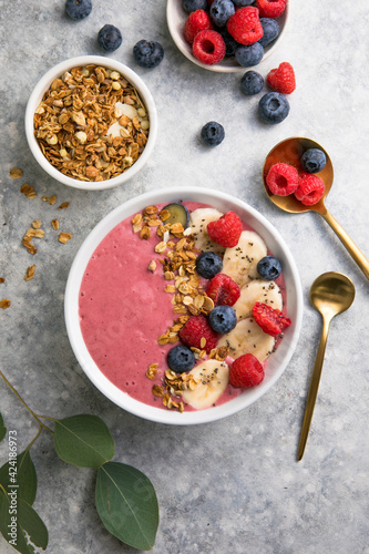 Summer acai smoothie bowls with raspberries, banana, blueberries, and granola on gray concrete background. Breakfast bowl with fruit and cereal, close-up, top view, space for text