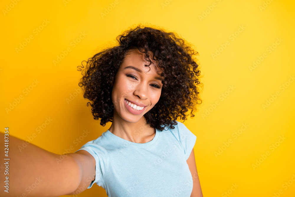 Photo of funny charming dark skin curly girl dressed blue t-shirt making selfie isolated yellow color background Photo of funny charming dark skin curly girl dressed blue t-shirt making selfie isolated yellow color background