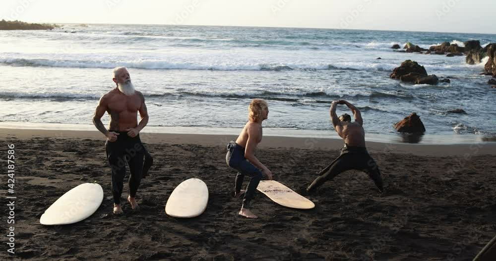 Multi generational surfer people doing warm up at the beach  before surf session- Multiracial men, lifestyle and sport concept