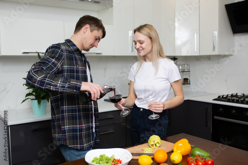 Young man pouring a glass of wine for his happy woman in the kitchen while cooking dinner together.