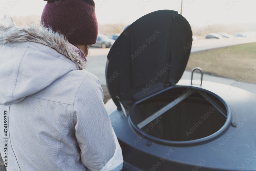 Woman throws garbage in the trash bin on the street.