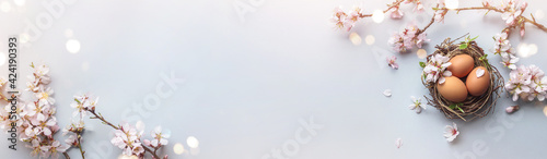 Easter eggs in nest and pink flowering sakura branches on light blue background. Happy Easter holiday, top view, flat lay