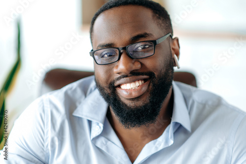 Close-up portrait of a handsome friendly intelligent African American man in formal blue shirt and eyeglasses, entrepreneur, agent or lawyer looking and smiling at the camera © Kateryna