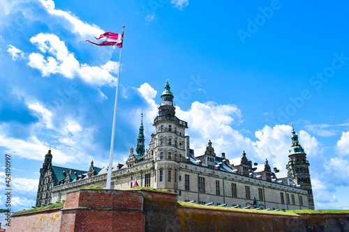 Medieval Kronborg castle and Danish flag on blue cloudy sky  background. Fortress is located on Oresund Strait shores of Baltic Sea. Helsingor, island Zealand, Denmark. photo