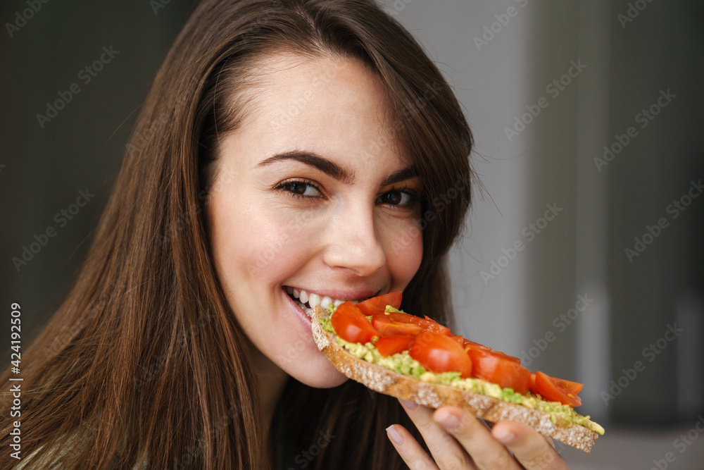 Young happy woman smiling while eating avocado toast indoors