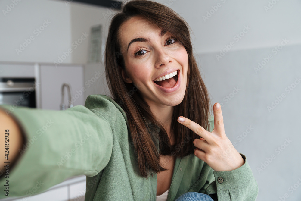 Young happy woman showing peace sign while taking selfie photo Young happy woman showing peace sign while taking selfie photo