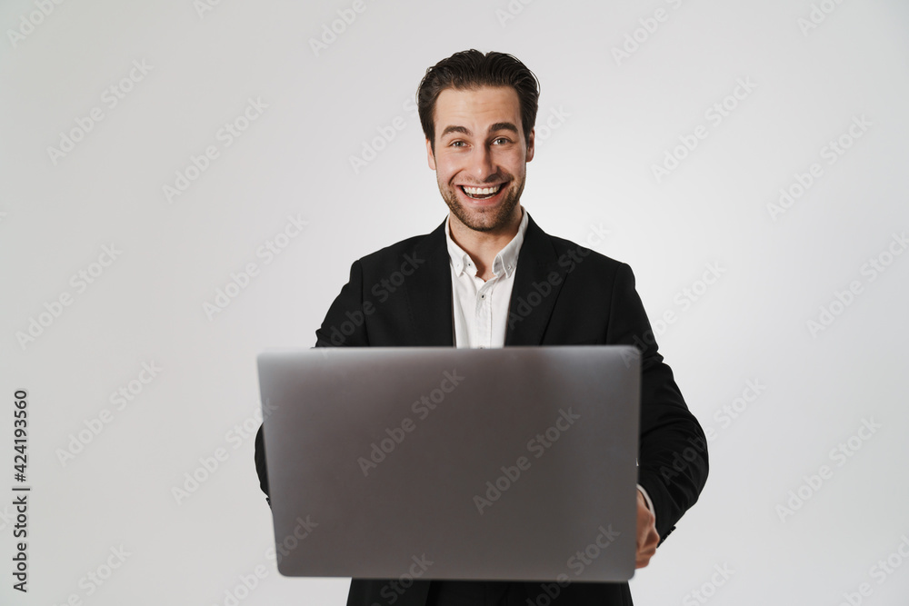 Unshaven brunette man in jacket smiling while using laptop Unshaven brunette man in jacket smiling while using laptop