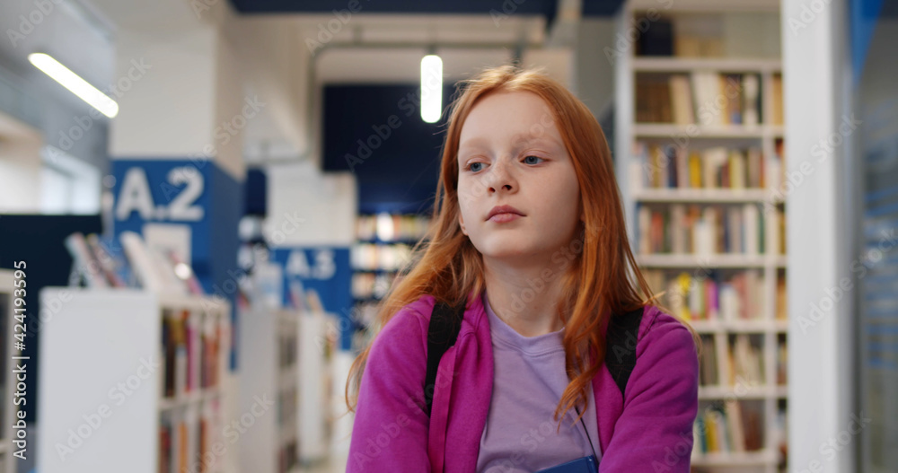 Schoolgirl walking in library choosing books for studying Schoolgirl walking in library choosing books for studying