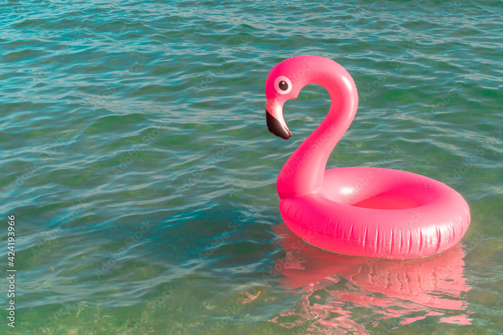 Fototapeta Summer time. Pink inflatable flamingo in blue ocean water for sea summer beach background. Funny bird toy for kids.