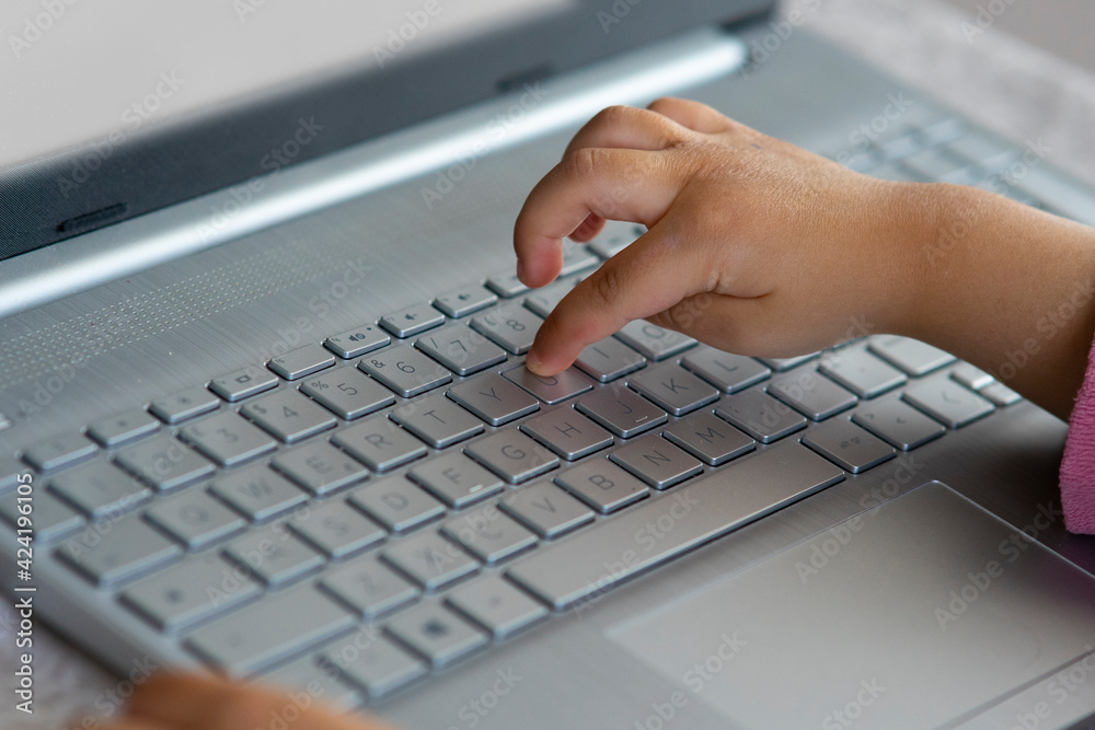 Hand of little girl using a notebook keyboard. Concept of distance learning or computer and technology addiction from childhood. Hand of little girl using a notebook keyboard. Concept of distance learning or computer and technology addiction from childhood.