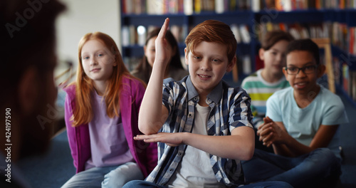 Redhead boy raising hand during lesson in school library