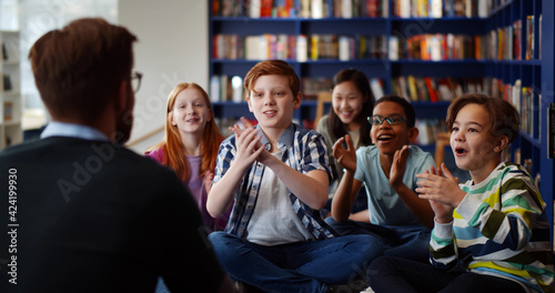 Schilderij op canvas Multiethnic group of kids sitting on floor near teacher and applauding