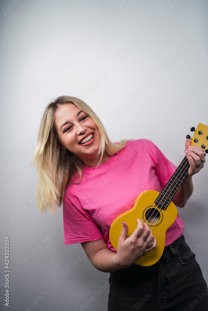 Fototapeta premium Young cheerful Caucasian female from Spain playing ukulele against a white wall