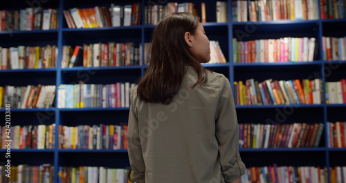 Back view of teen girl looking at bookshelves in library