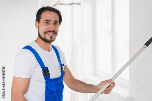 Handsome man in overalls paints the wall with a roller