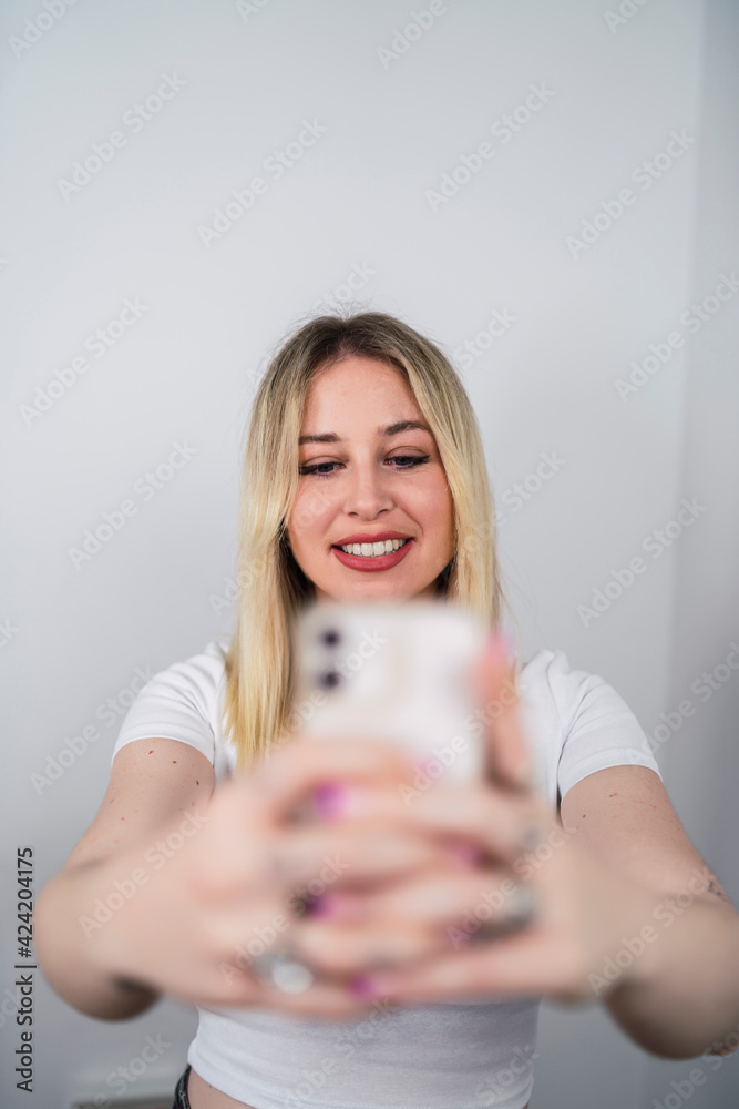 Chica rubia risueña usando smartphone y sonriendo sobre fondo blanco Chica rubia risueña usando smartphone y sonriendo sobre fondo blanco