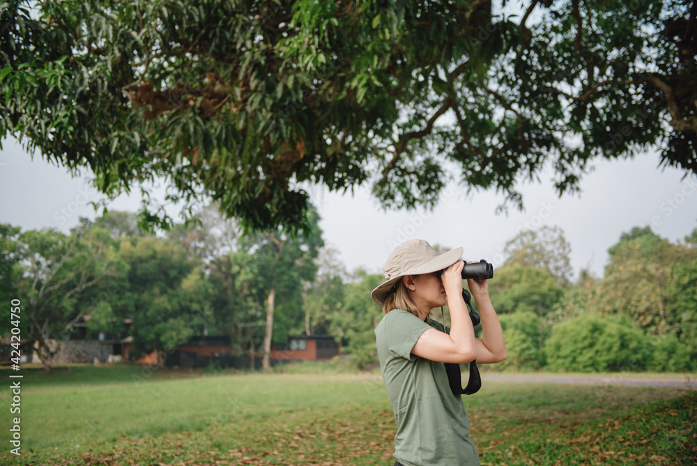Young asian girl with hiking hat looks through binoculars between a travel.